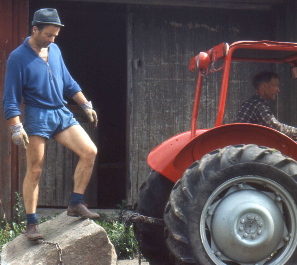 Foto av Jan Halvard Arntzen på sten fra grunnmuren på Sika, som måtte fjernes for å støpe såle. Erling Johansen fører traktoren. Bildet er tatt i 1968 og Jan er 38 år. Minneordforfatter Rolf Utgård var selv med på arbeidet, 18 år gammel.